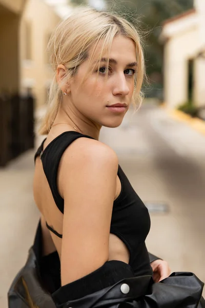 Portrait of blonde young woman in black tank top looking at camera outdoors — Stock Photo