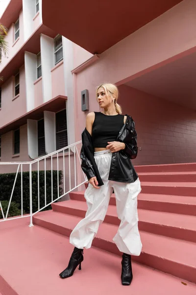 Pleine longueur de jeune femme blonde en débardeur noir et pantalon cargo debout sur des escaliers roses à Miami — Photo de stock