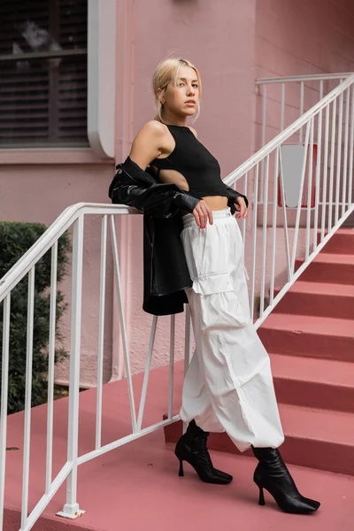 Pleine longueur de femme blonde en débardeur noir et pantalon cargo debout sur des escaliers roses à Miami — Photo de stock