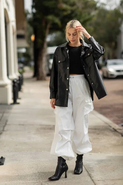 Comprimento total de mulher loira em jaqueta de camisa de couro e calças de carga andando na rua urbana em Miami — Fotografia de Stock