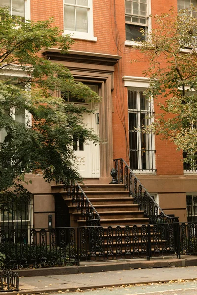 Цегляний будинок з білими вікнами і вхід зі сходами біля осінніх дерев на вулиці в Нью-Йорку. — стокове фото