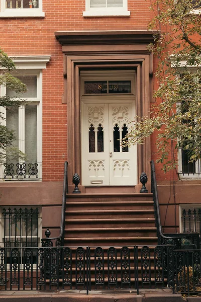 Кирпичное здание с белой дверью и лестницей с металлическими перилами и забором в Нью-Йорке — стоковое фото
