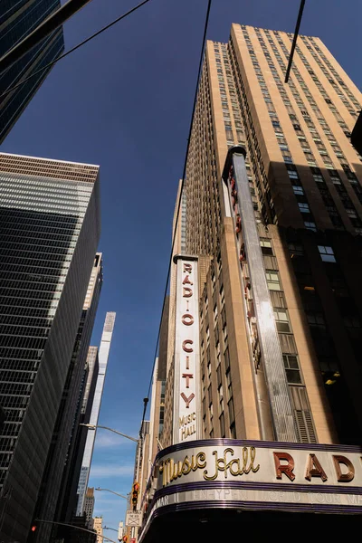 НЬЮ-ЙОРК, США - 13 ОКТЯБРЯ 2022 года: низкоугольный вид на мюзик-холл Radio City рядом с современными зданиями на фоне голубого неба — стоковое фото