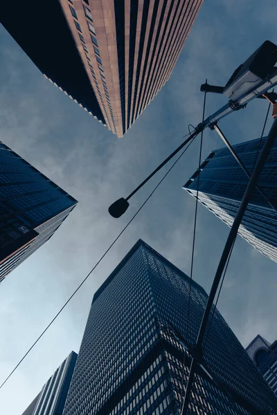 Вид снизу уличной лампы рядом с небоскребами против голубого и облачного неба в Нью-Йорке — стоковое фото
