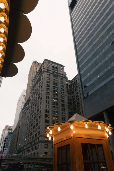 Телефонная будка со светящимися лампами возле зданий на вечерней улице Манхэттена в Нью-Йорке — стоковое фото