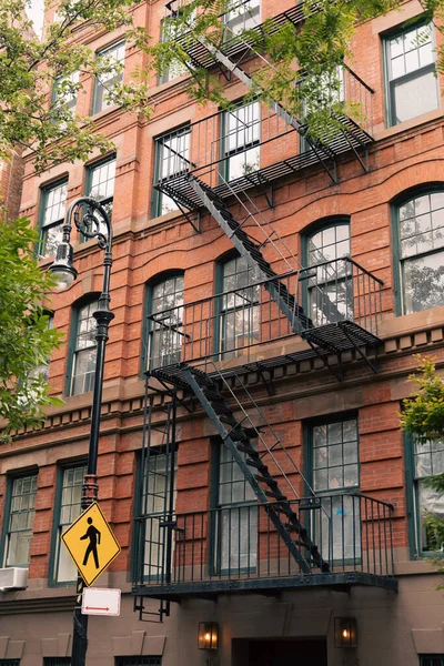 Edifício de tijolos com varandas de metal e escadas de escada de incêndio perto de lanterna com sinal de travessia de pedestres em Nova York — Fotografia de Stock