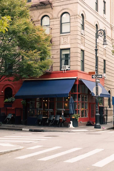 Серое здание с кафе на углу рядом с фонарем и пешеходным переходом по дороге в Нью-Йорке — стоковое фото
