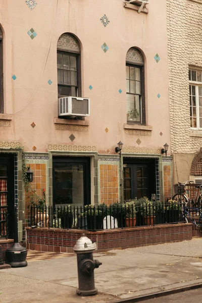 Viejo edificio con ventanas de arco cerca de valla de metal y macetas con plantas en la ciudad de Nueva York - foto de stock