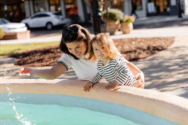 Glückliche Mutter blickt auf Wasser in Brunnen neben Kleinkind Tochter auf Straße in Miami — Stockfoto