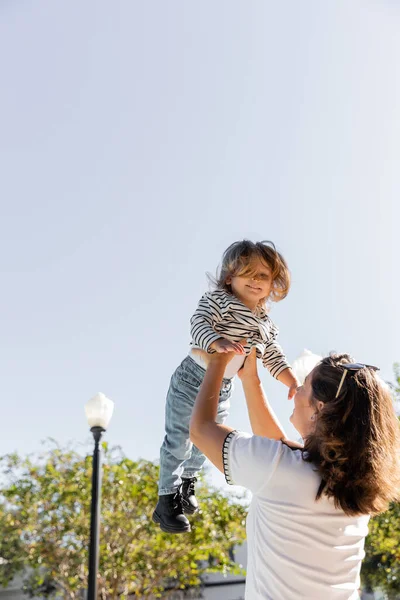 Brunette mother in sunglasses lifting happy toddler daughter on street in Miami — Stock Photo