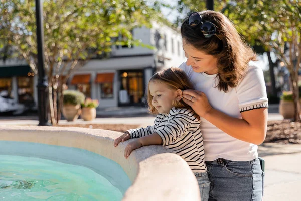Glückliche Mutter mit Sonnenbrille blickt auf süße Kleinkind-Tochter in der Nähe eines Brunnens in Miami — Stockfoto