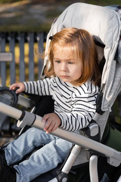 Toddler kid in striped long sleeve shirt sitting in baby stroller — Stock Photo