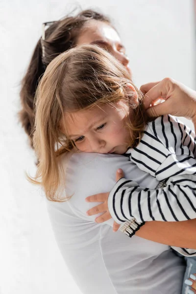 Заботливая мать утешает малышку в полосатой рубашке с длинным рукавом — стоковое фото