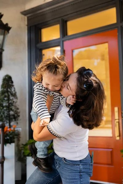Brunette mother lifting and kissing cheek of toddler daughter near house in Miami — Stock Photo