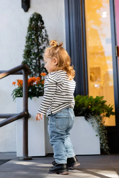 Side view of baby girl in long sleeve shirt and blue jeans standing near house in Miami — Stock Photo