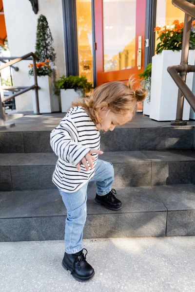 Bébé fille en chemise à manches longues et jeans bleus debout sur les escaliers du porche près de la maison à Miami — Photo de stock
