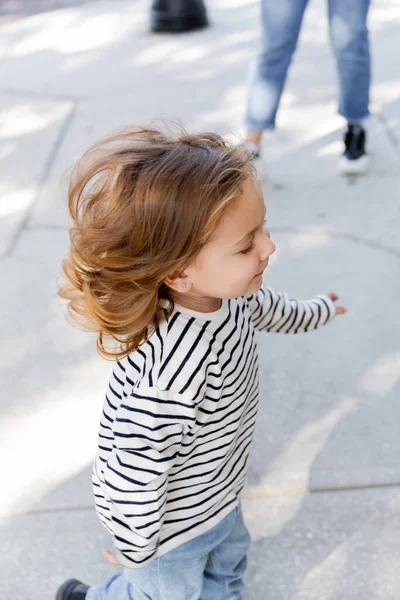 Щаслива дівчинка-малюк в сорочці з довгим рукавом біжить біля матері на розмитому фоні — стокове фото