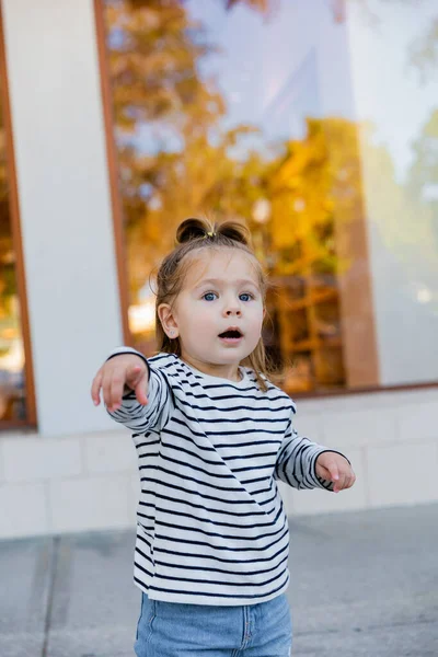 Amazed baby girl in striped long sleeve shirt pointing with finger outdoors — Stock Photo