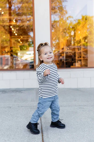 Повний зріст щасливої дівчини в джинсах і сорочці з довгими рукавами, що стоїть біля магазину в Маямі. — стокове фото