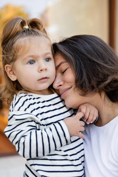 Portrait of caring mother hugging toddler girl in striped long sleeve shirt — Stock Photo