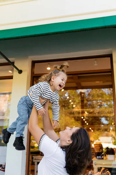 Fröhliche Mutter hebt glückliches Baby-Mädchen nahe Schaufenster eines Geschäfts in Miami — Stockfoto
