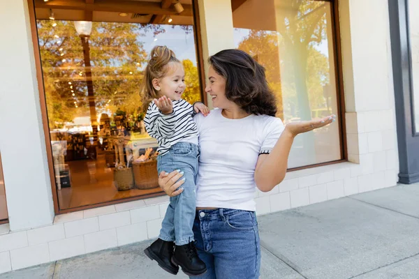 Glückliche Mutter hält Baby-Tochter in der Nähe von Schaufenster eines Geschäfts in Miami in den Armen — Stockfoto