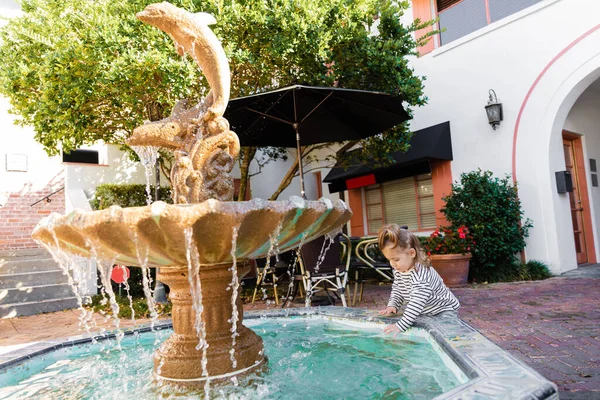 Tout-petit fille en chemise à manches longues rayée mouiller les mains dans l'eau de la fontaine à Miami — Photo de stock