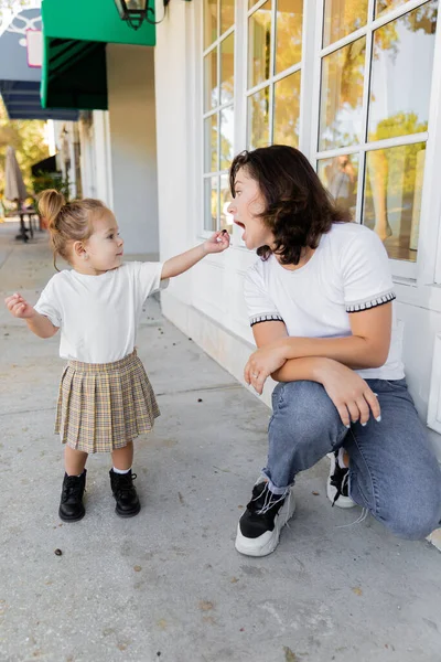 Toddler girl in skirt and t-shirt holding acorn near mother with opened mouth — Stock Photo