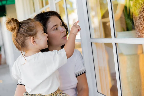 Morena mãe segurando em braços bebê filha enquanto olha para janelas de casa em Miami — Fotografia de Stock
