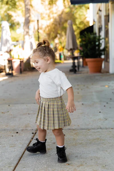 Full length of cheerful toddler girl in skirt and white t-shirt standing on street in Florida — Stock Photo