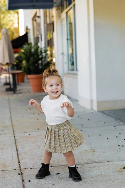 Full length of positive toddler girl in skirt and white t-shirt standing on street in Miami — Stock Photo