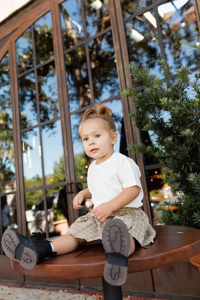 Volle Länge des Kleinkindes in Rock und weißem T-Shirt sitzt auf einem Bistrotisch in der Nähe eines Cafés in Miami — Stockfoto