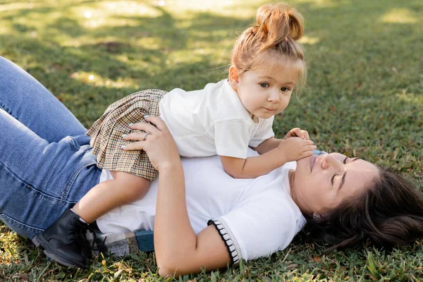 Брюнетка мать лежит на зеленой лужайке с малышом девочка — стоковое фото