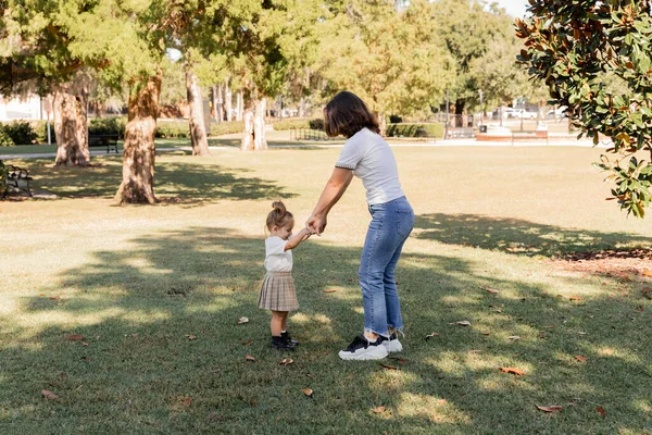 Full length of mother in jeans holding hands with toddler daughter in park of Miami — Stock Photo