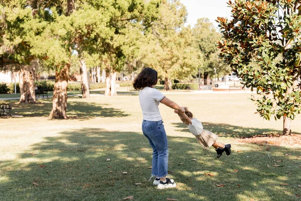 Pleine longueur de brunette mère en jeans jouer avec tout-petit fille dans le parc de Miami — Photo de stock