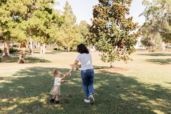 Full length of brunette mother in jeans playing with happy toddler daughter in park of Miami — Stock Photo