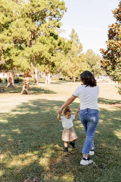 Brunette mother holding hands with happy toddler daughter while playing in park of Miami — Stock Photo