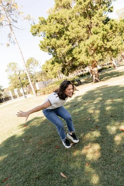 Femme positive en jeans debout avec les mains tendues dans le parc vert de Miami — Photo de stock