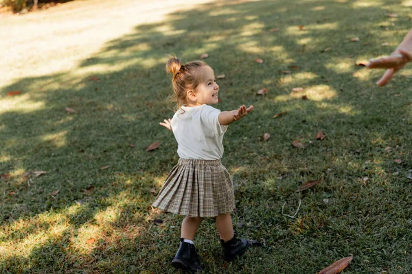 Счастливая девочка, стоящая с протянутыми руками во время игры в парке — стоковое фото