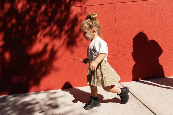 Mädchen in kariertem Rock und weißem T-Shirt läuft in der Nähe eines Gebäudes mit roter Wand — Stockfoto