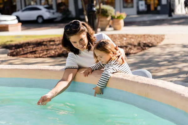 Mère heureuse regardant l'eau claire dans la fontaine près de sa fille à Miami — Photo de stock