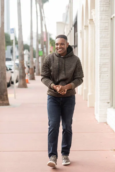 Voller Länge von fröhlichen afrikanisch-amerikanischen Mann in Kapuzenpulli und Jeans zu Fuß auf der Straße in Miami — Stockfoto