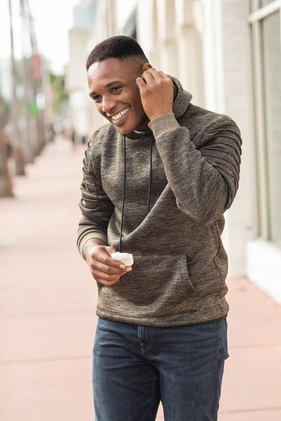 Sonriente afroamericano en sudadera con capucha con estuche para auriculares en la calle en Miami - foto de stock