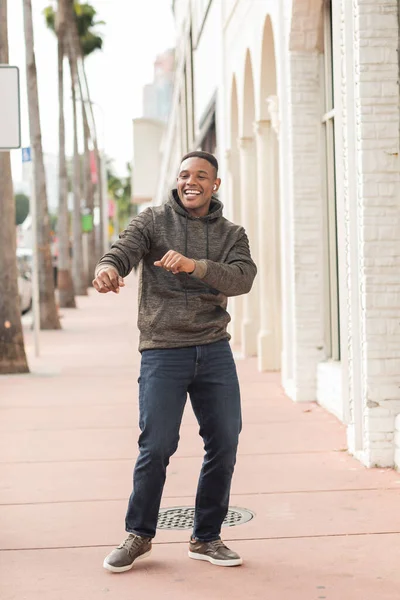 Hombre afroamericano feliz en auriculares inalámbricos que se divierten en la calle en Miami - foto de stock