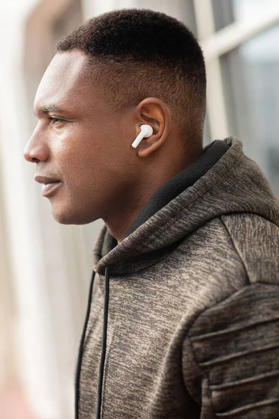 Seitenansicht eines afrikanisch-amerikanischen Mannes in drahtlosem Kopfhörer, der im Freien Musik hört — Stockfoto