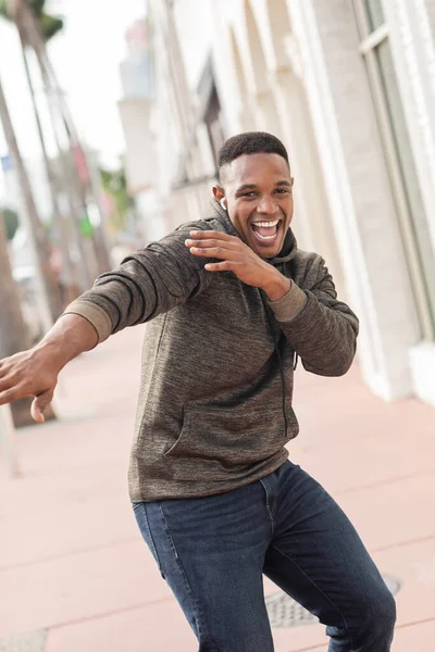 Excité homme afro-américain en écouteur sans fil écouter de la musique et danser dans la rue à Miami — Photo de stock