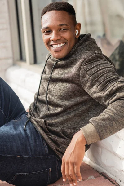 Веселий афроамериканський чоловік слухає музику в бездротових навушниках і сидить на вулиці — стокове фото