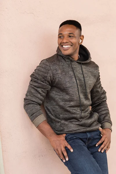 Cheerful african american man in wireless earphone standing near wall — Stock Photo