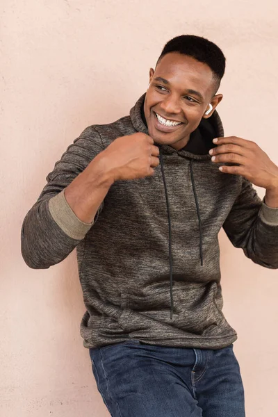 Веселый африканский американец в беспроводном наушнике слушает музыку у стены — стоковое фото