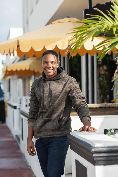 Веселий афроамериканський чоловік у бездротових навушниках, що стоять біля відкритого бістро — стокове фото